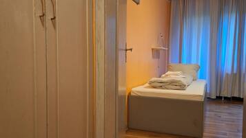 Un dormitorio con cama, suelo de madera, armario y ventana con cortinas.