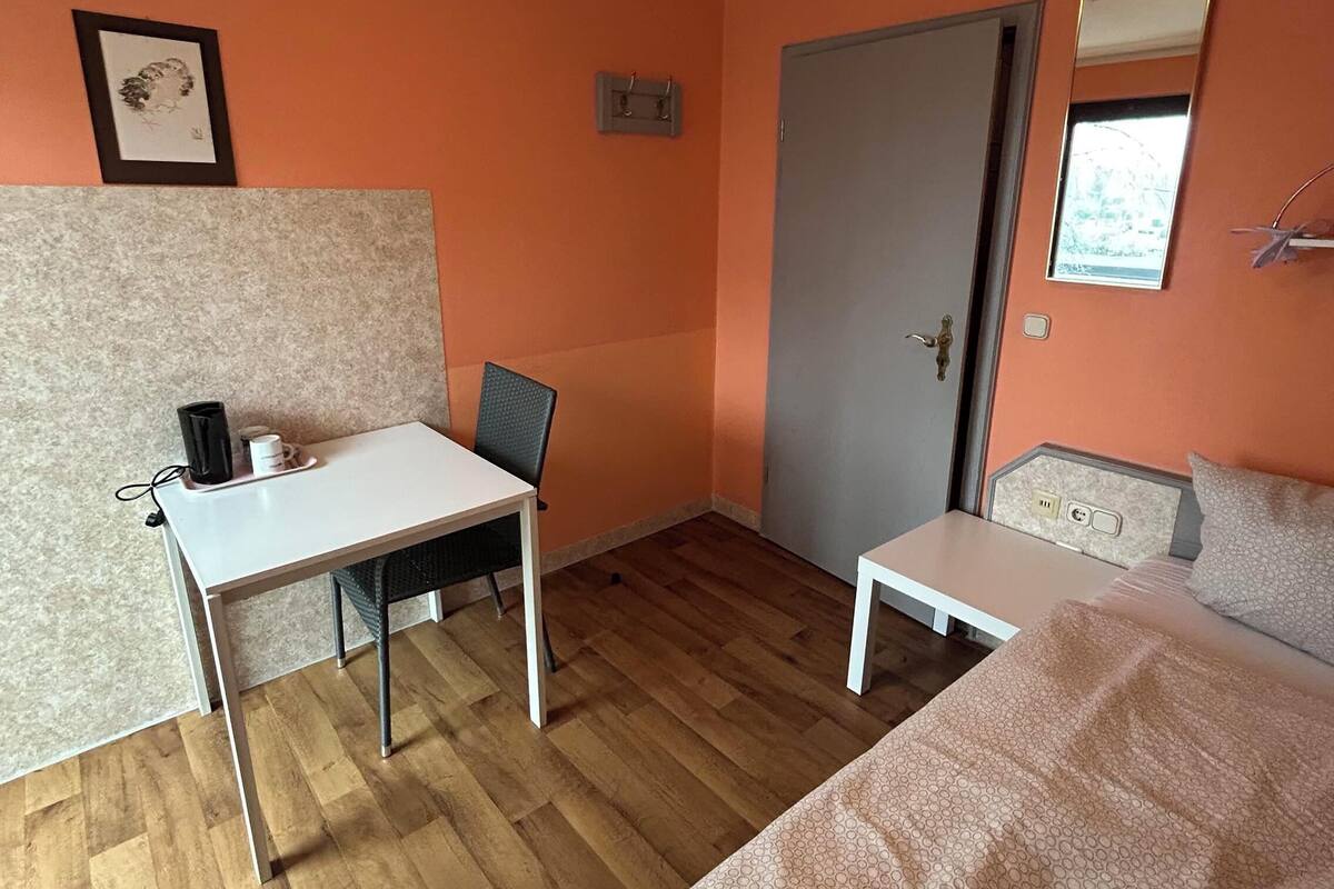 Une pièce comprenant un lit, un bureau et une chaise. Il y a une porte et une petite fenêtre.