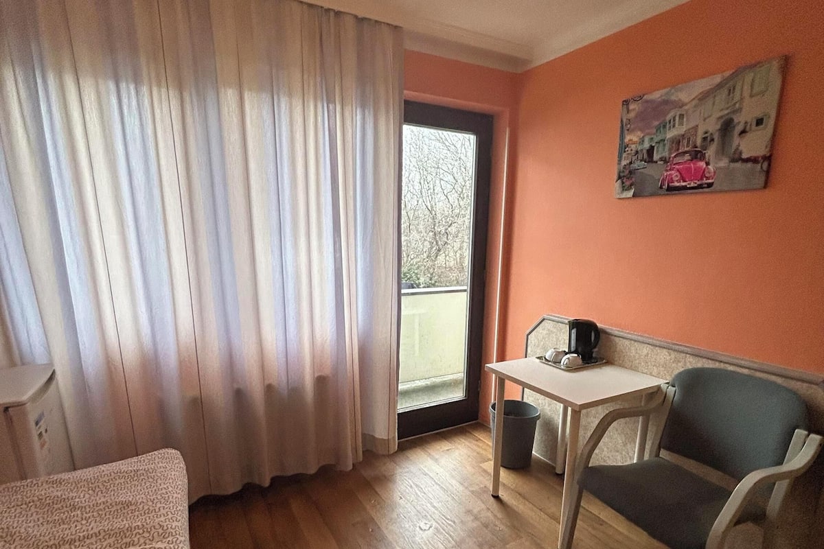 Une pièce avec un plancher en bois, un canapé, une table avec une chaise, une fenêtre avec des rideaux et un tableau au mur.