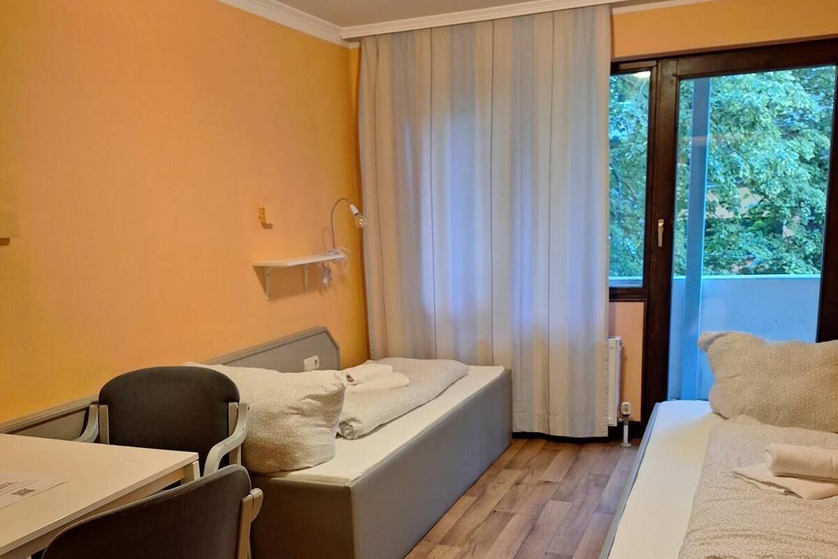 Une chambre d’hôtel avec un lit, un bureau, une chaise et une vue sur la verdure par la fenêtre.