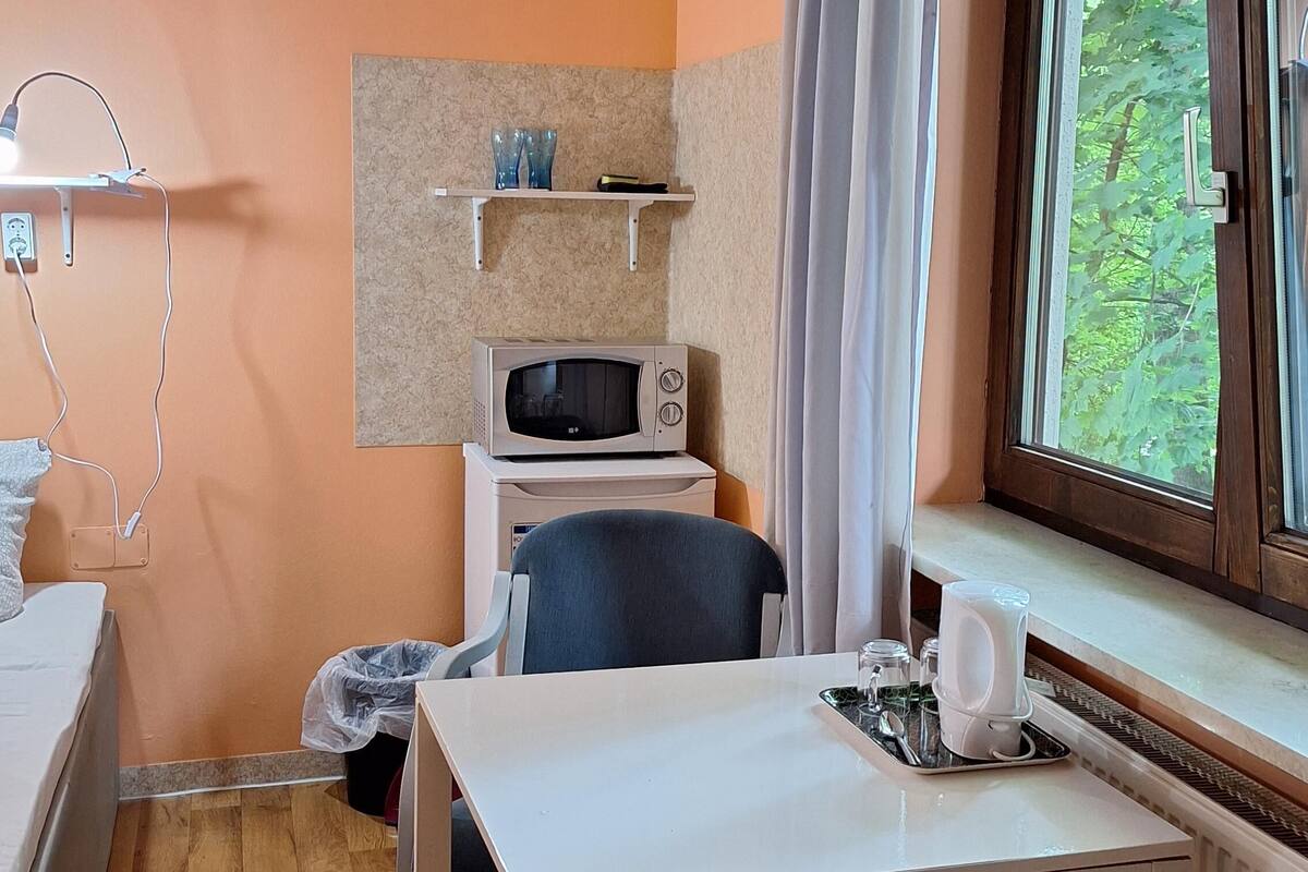 Une chambre compacte comprenant un lit, un four à micro-ondes, une petite table avec un plateau, et une fenêtre avec des rideaux.
