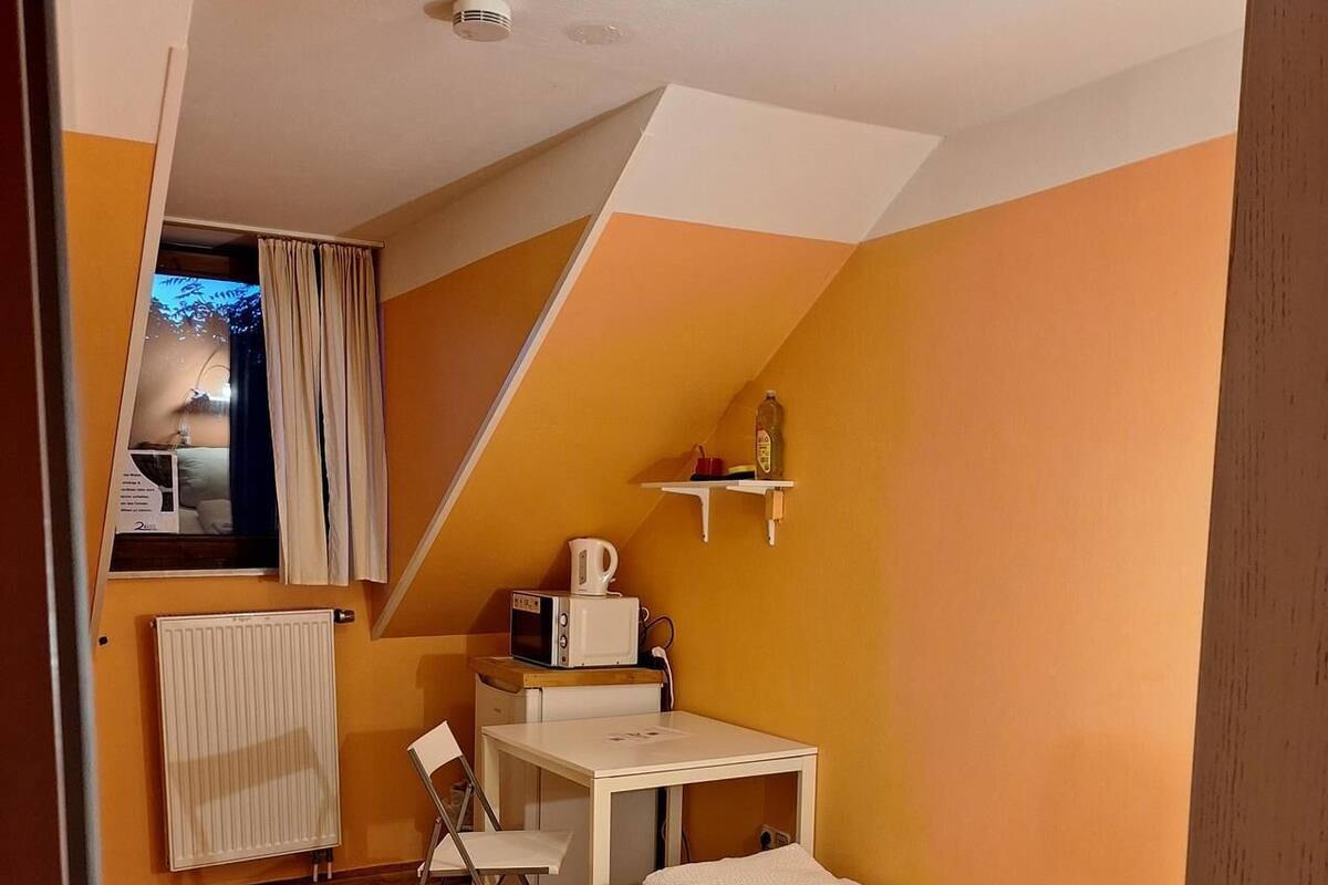 Une petite pièce comprenant un lit, un bureau, une chaise et un radiateur.