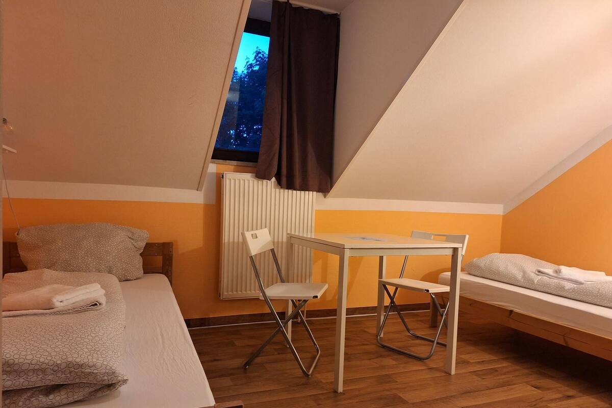 Une petite pièce agréable, avec un plafond en pente, un lit simple, une petite table et une chaise.