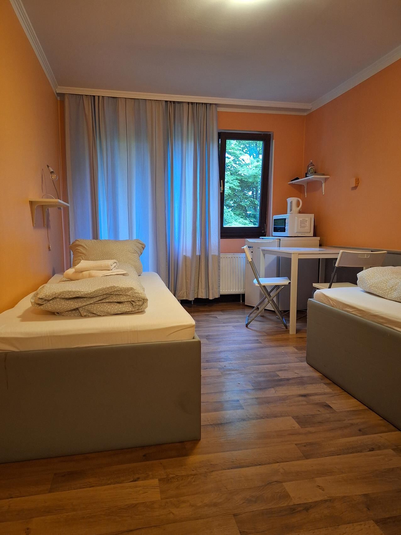 Una habitación con dos camas, un escritorio, una silla, una ventana con cortinas y un radiador.