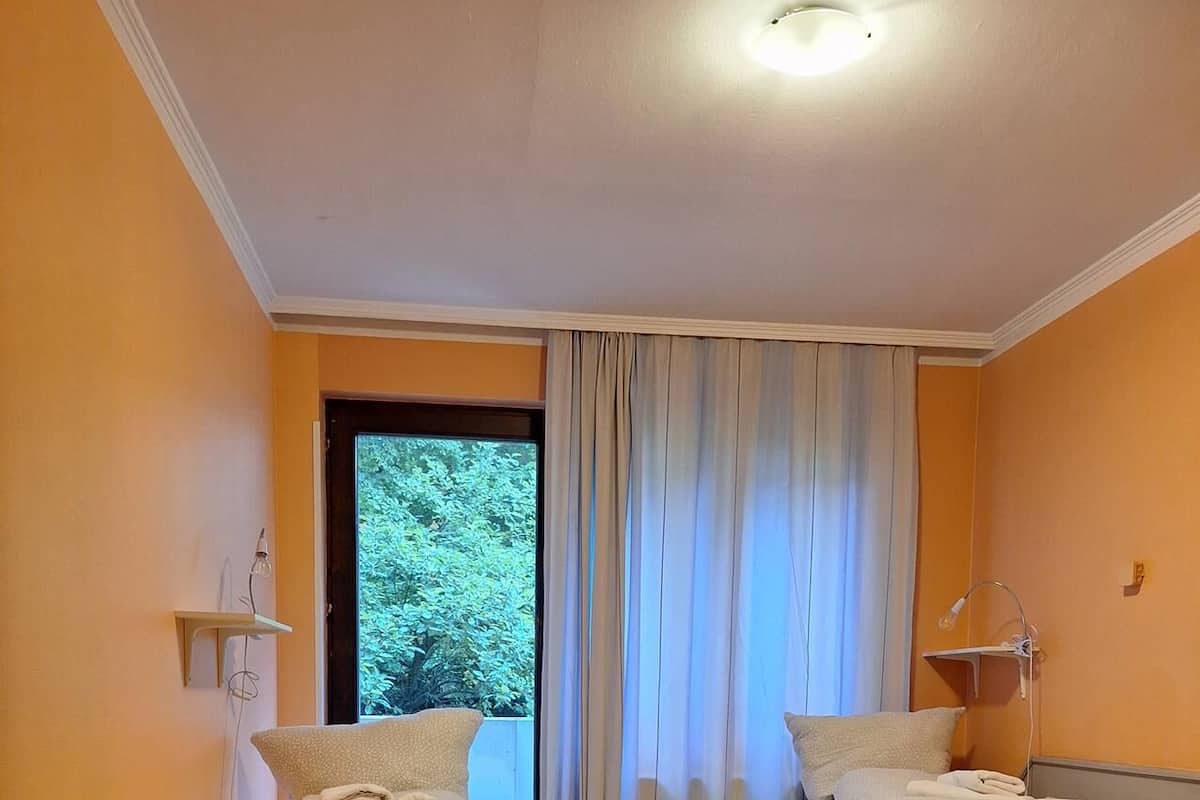 Une chambre avec deux lits, une fenêtre avec des rideaux, un plancher en bois et un luminaire au plafond.