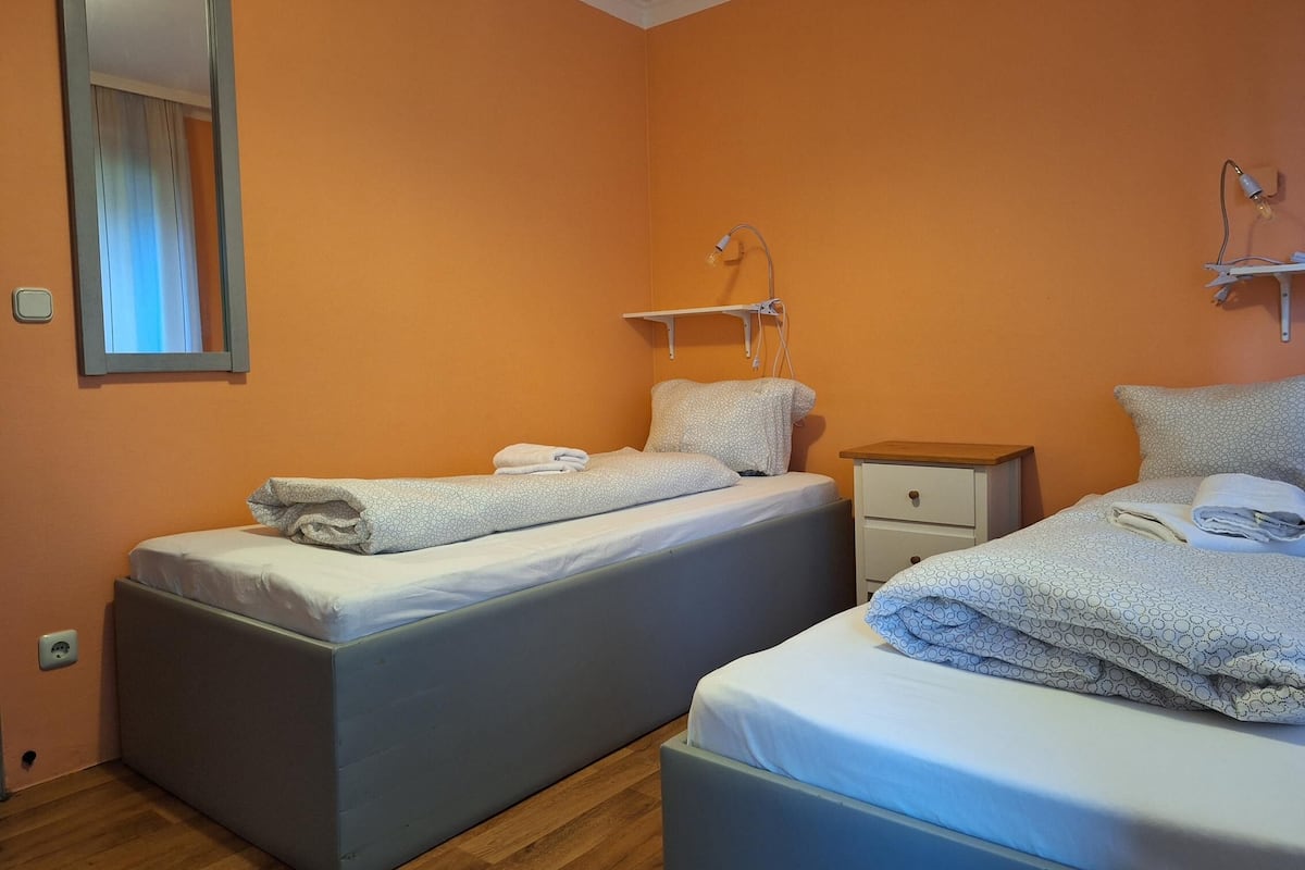 Une chambre avec deux lits, une table de chevet, une commode, un miroir et une lampe fixée au mur.