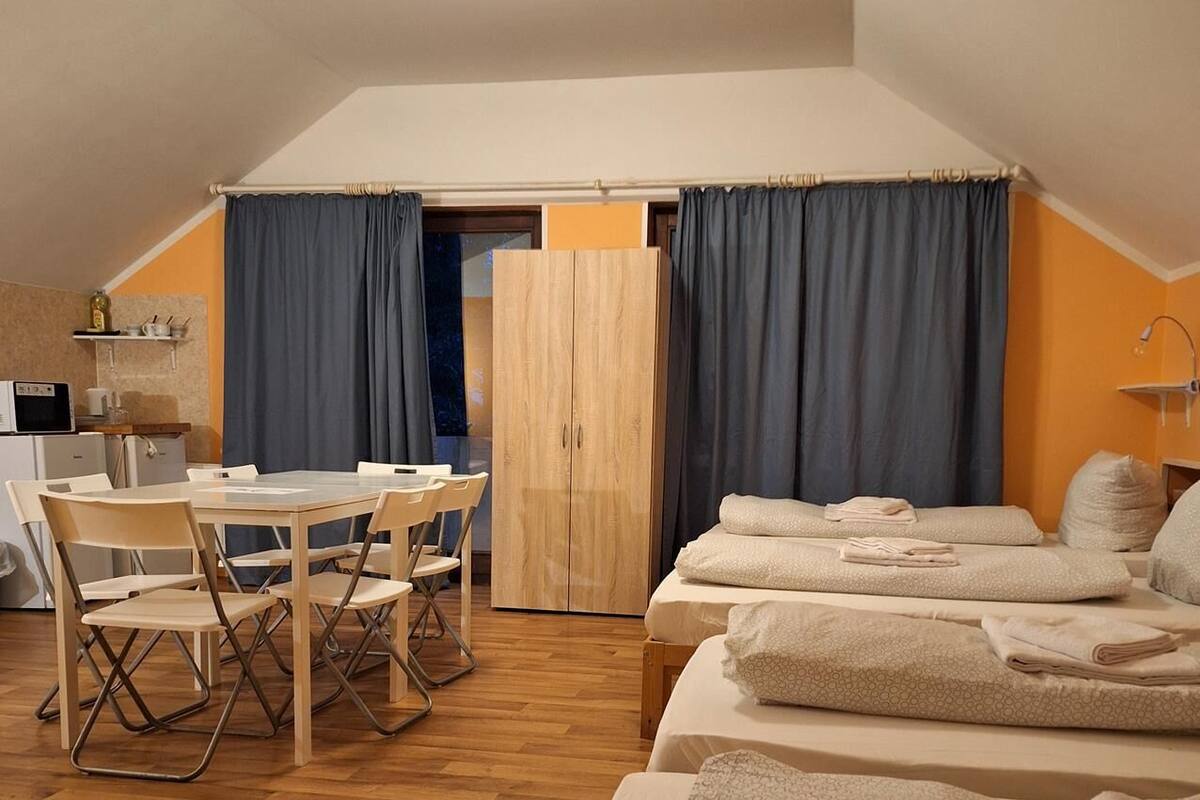 Une pièce chaleureuse et bien éclairée, avec une table à manger, des chaises et deux lits où les serviettes sont soigneusement pliées.
