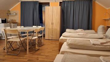 Quarto aconchegante e bem iluminado, com uma mesa de jantar, cadeiras e duas camas com toalhas dobradas.