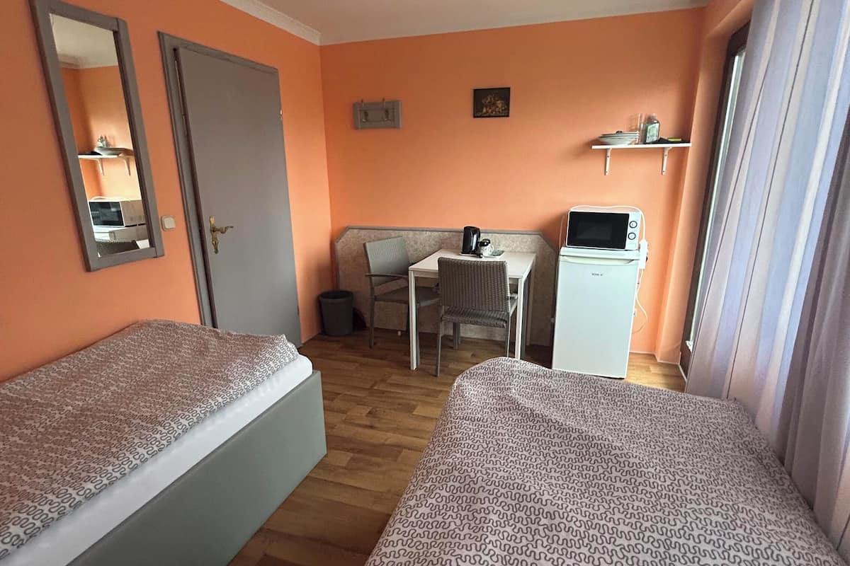 Une chambre d’hôtel avec deux lits simples, une petite table, une bouilloire, un four à micro-ondes et une chaise.