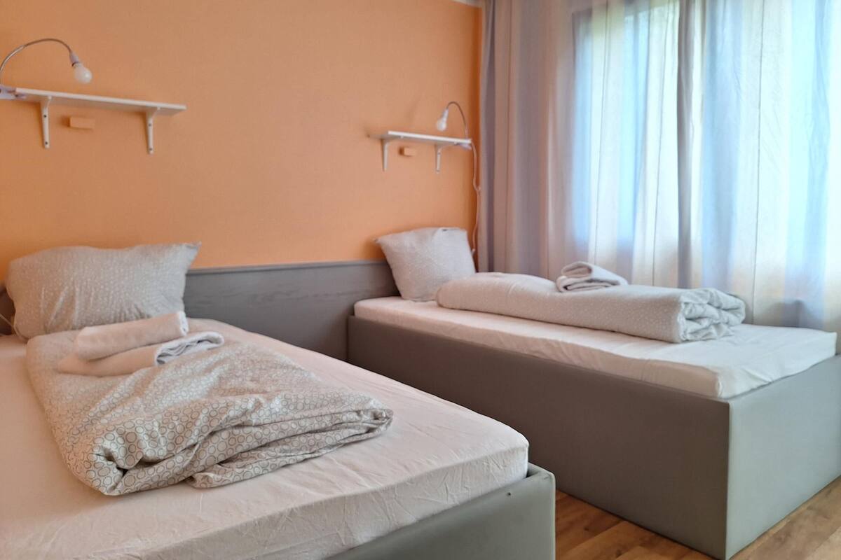 Une chambre d’hôtel avec deux lits, chacun équipé d’un oreiller et d’une serviette pliée. Des appliques murales sont fixées au-dessus de chaque lit.