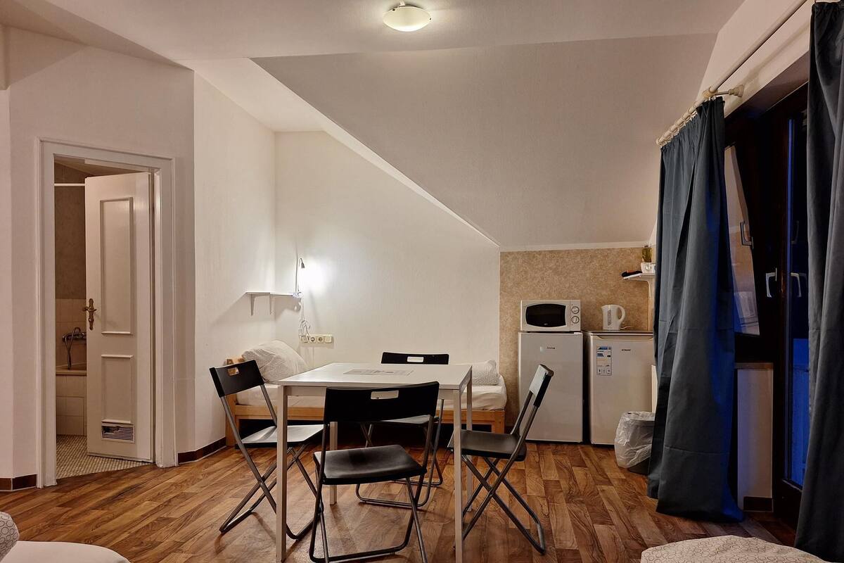 Une chambre d’hôtel compacte comprenant une table à manger, des chaises, un lit, une petite kitchenette et une salle de bain visible à travers une porte ouverte.