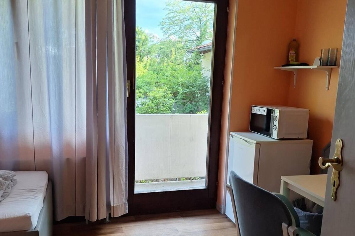 Une chambre avec un lit, un bureau, une chaise, un four à micro-ondes et une vue sur la verdure.