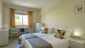 A hotel room with two beds, a desk, a chair, a wardrobe, and a window with curtains.