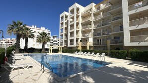 A modern hotel with a swimming pool, multiple balconies, and palm trees.