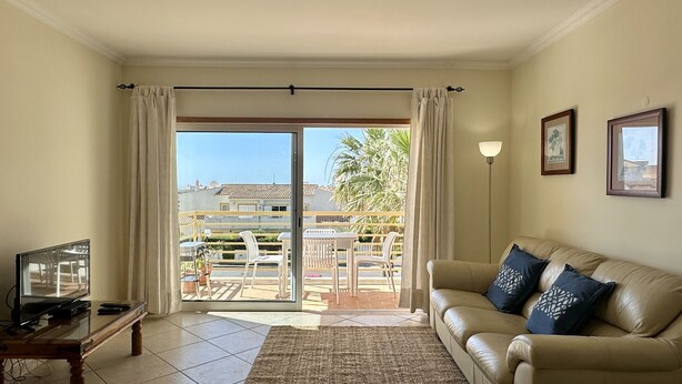 A living room with a sofa, a television, and a view of a balcony with outdoor furniture.