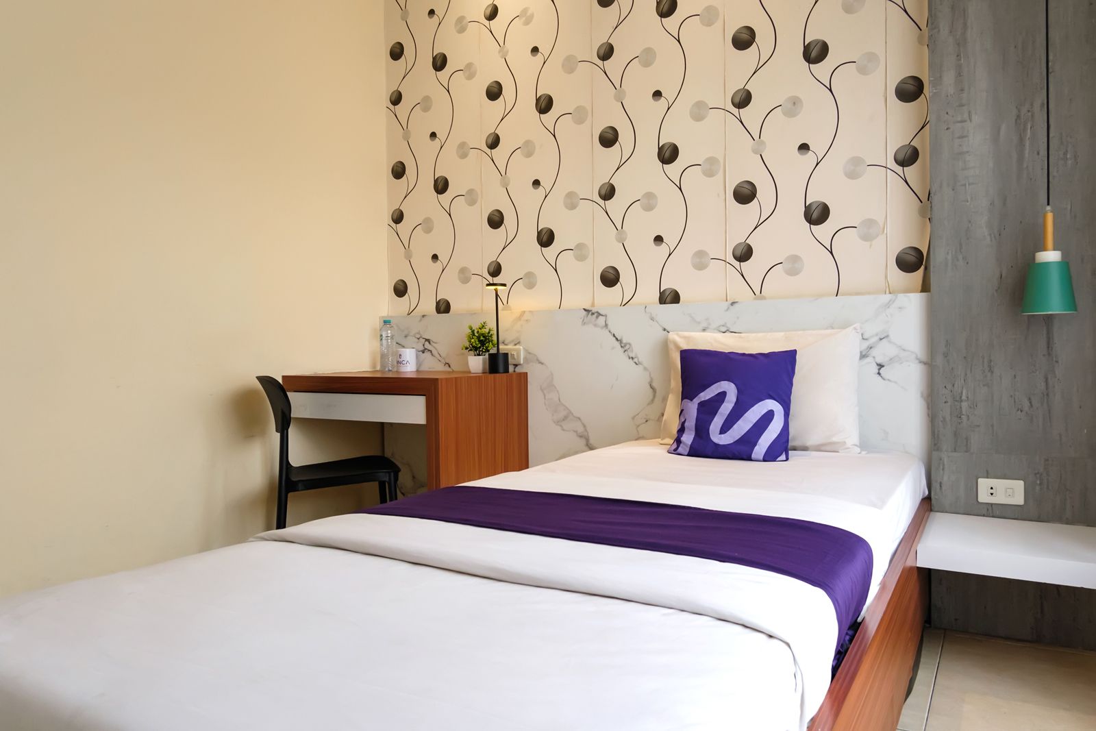 A hotel room with a bed, a desk, and a wall with a decorative pattern.