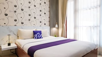 Une chambre à coucher moderne avec un grand lit, une table de chevet, une lampe et une vue sur l’extérieur à travers des rideaux légers.