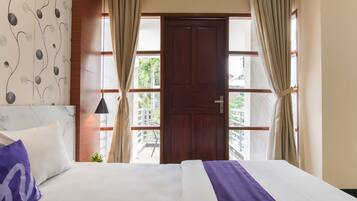A hotel room with a bed, curtains, a door, and a view of the outside.