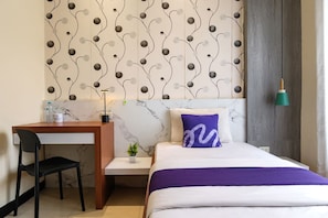 A hotel room with a bed, a desk, a chair, a small plant, and a wall with a decorative pattern. - INNCA Jatidiri Villa, Semarang (Semarang)