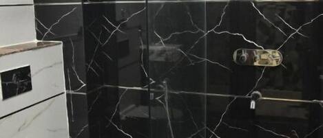 Un baño con ducha de vidrio, inodoro blanco y salpicadero de mármol.
