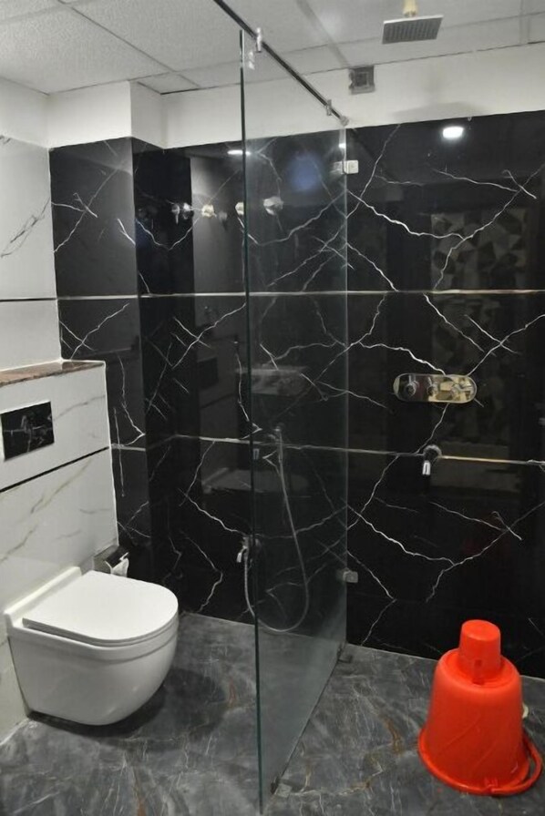 A bathroom with a glass-enclosed shower, a white toilet, and a marble backsplash.