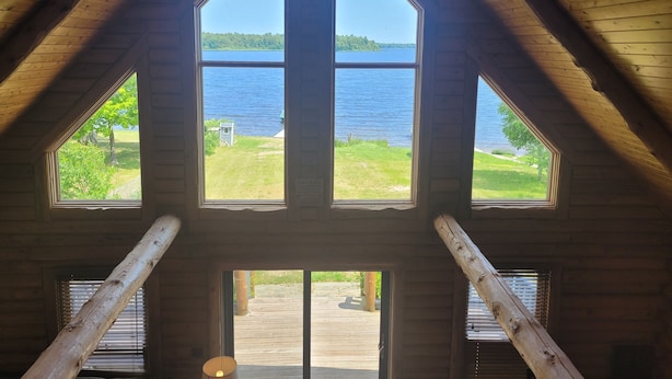 Une pièce dotée d’une grande fenêtre donnant sur un lac, de poutres en bois et offrant une vue sur l’extérieur.