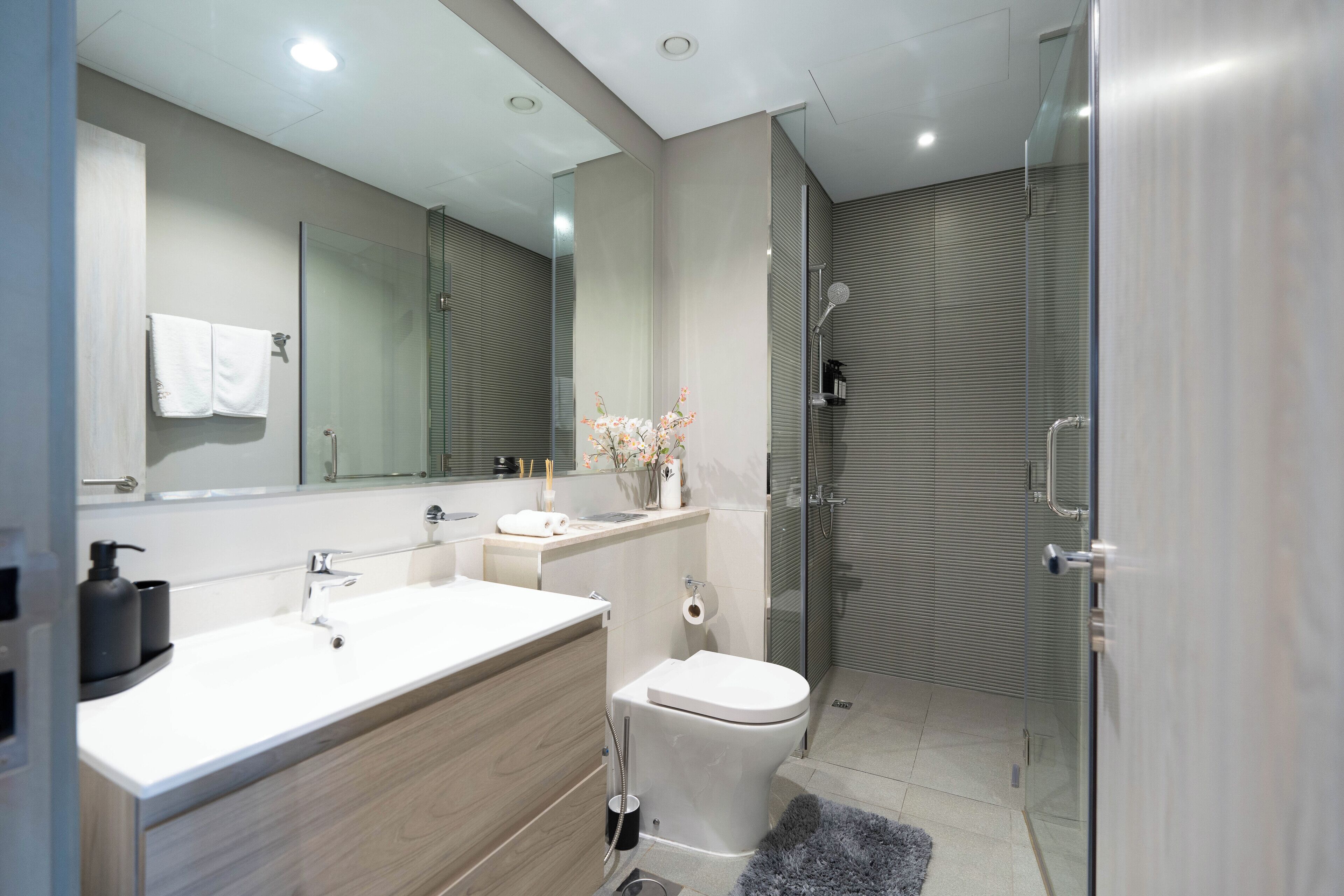 Une salle de bain moderne avec un grand miroir, un lavabo blanc, des toilettes et une douche séparée par une paroi de verre.