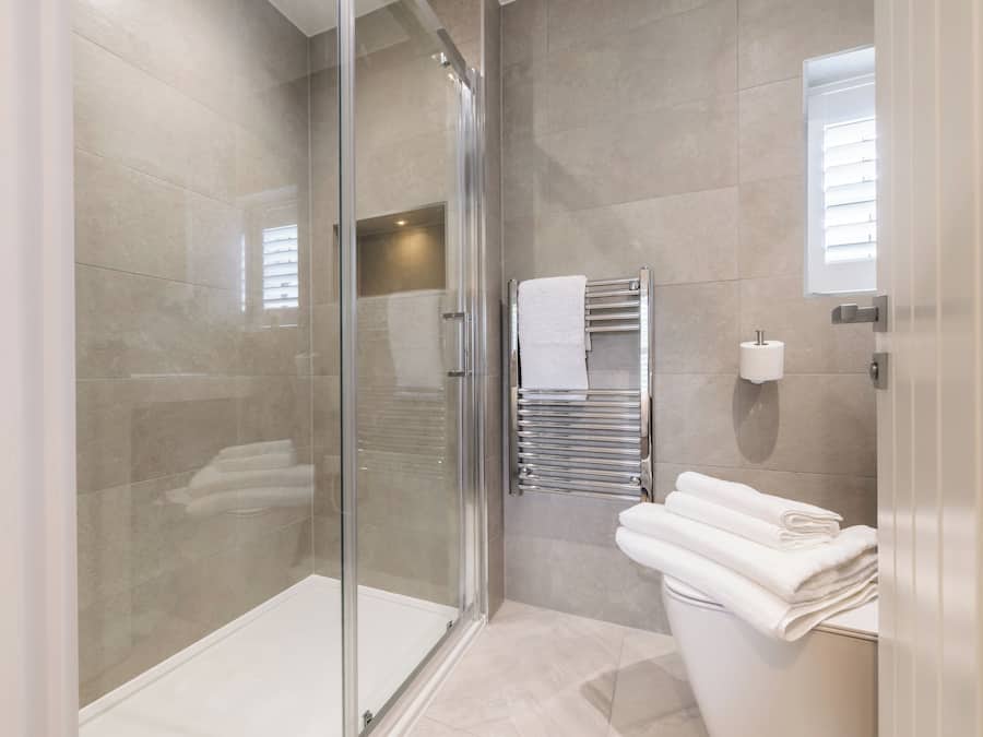 Un baño moderno con cabina de ducha de vidrio, un inodoro y un perchero con toallas dobladas.