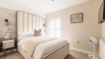 A bedroom with a bed, bedside table, wall art, window, and a standing fan.