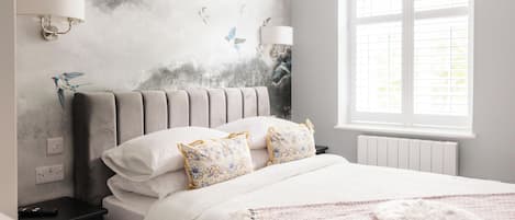 Un dormitorio con cabecera tapizada en gris, ropa de cama blanca y un mural decorativo en la pared.