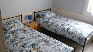 Una habitación con dos camas individuales, una mesita de noche de madera con lámpara y una ventana con vistas al follaje.