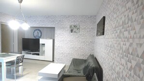 Una sala de estar moderna con un sofá, una mesa de comedor con sillas, un televisor y una zona de cocina.