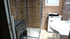 Un baño pequeño con ducha de vidrio, lavadora y lavamanos con espejo.