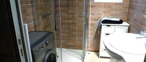 Un baño pequeño con ducha de vidrio, lavadora y lavamanos con espejo.