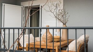 Un balcón con una mesa y sillas de madera, una planta en maceta y vista al interior.