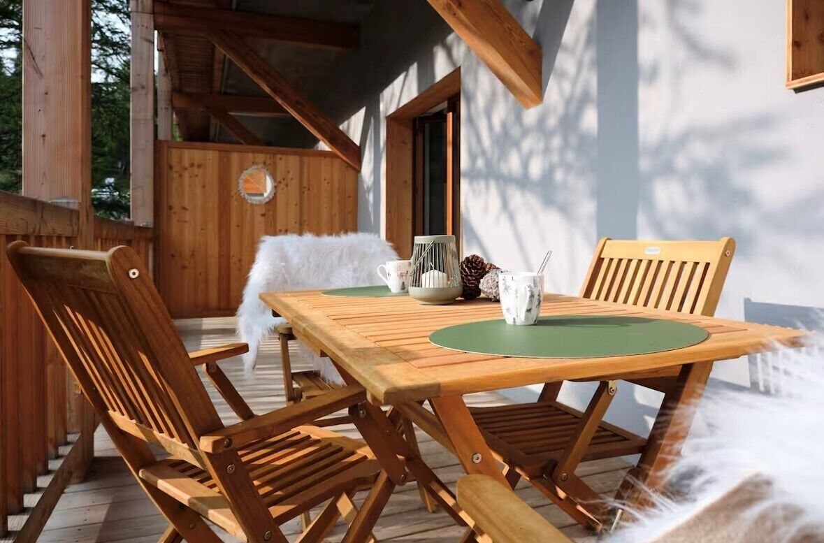 A wooden deck with a table and chairs, a white fluffy object, and a wooden cabin structure in the background.