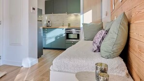 A modern room with a bed, a small table with decorative items, and a kitchen in the background. - Superb Cosy Studio, Terrace, parking, ski locker close to slopes. (Vars)