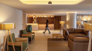 A modern hotel lobby with a reception desk, seating area, and a person walking through.