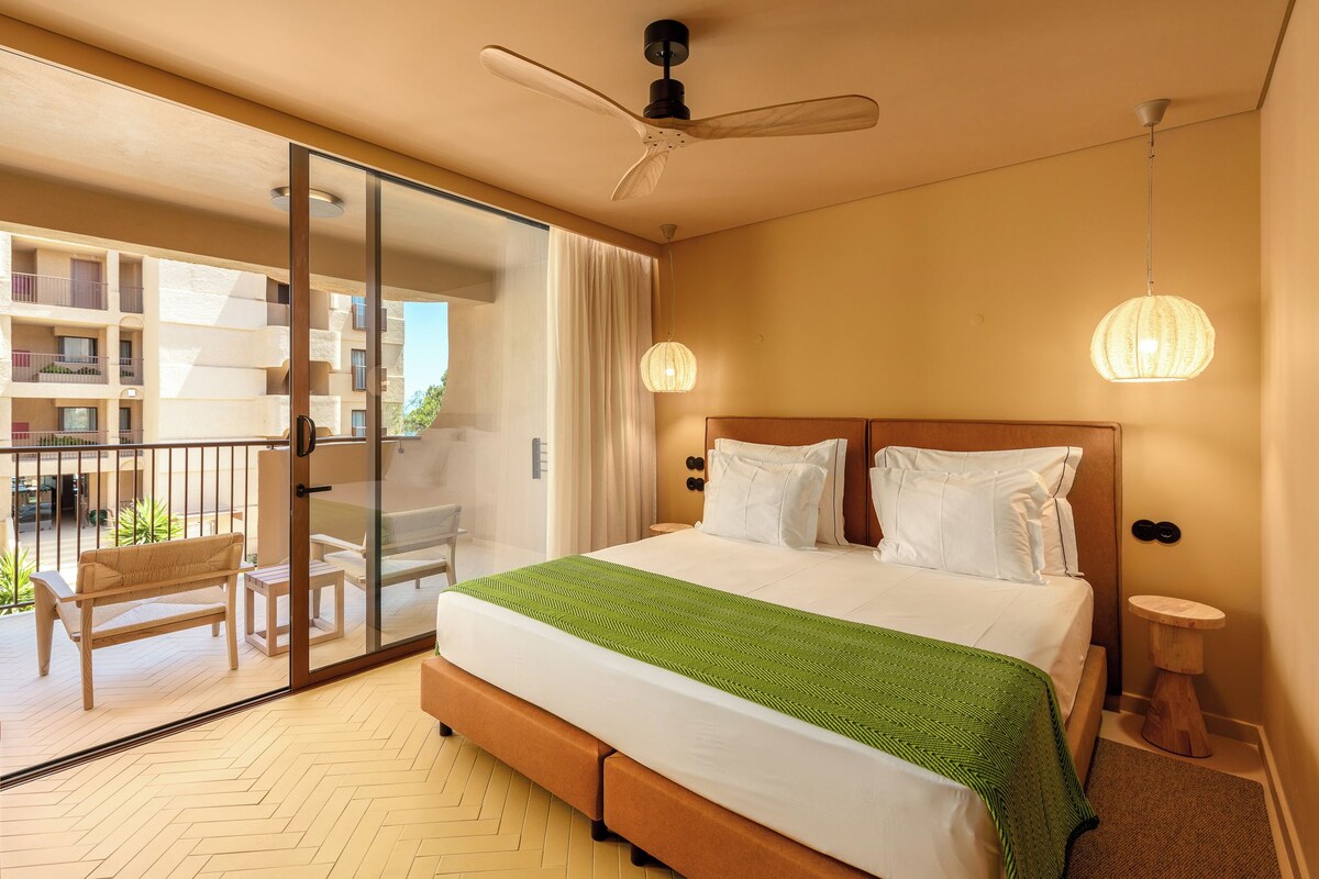 A hotel room with a bed, a balcony, a ceiling fan, and a hanging light fixture.