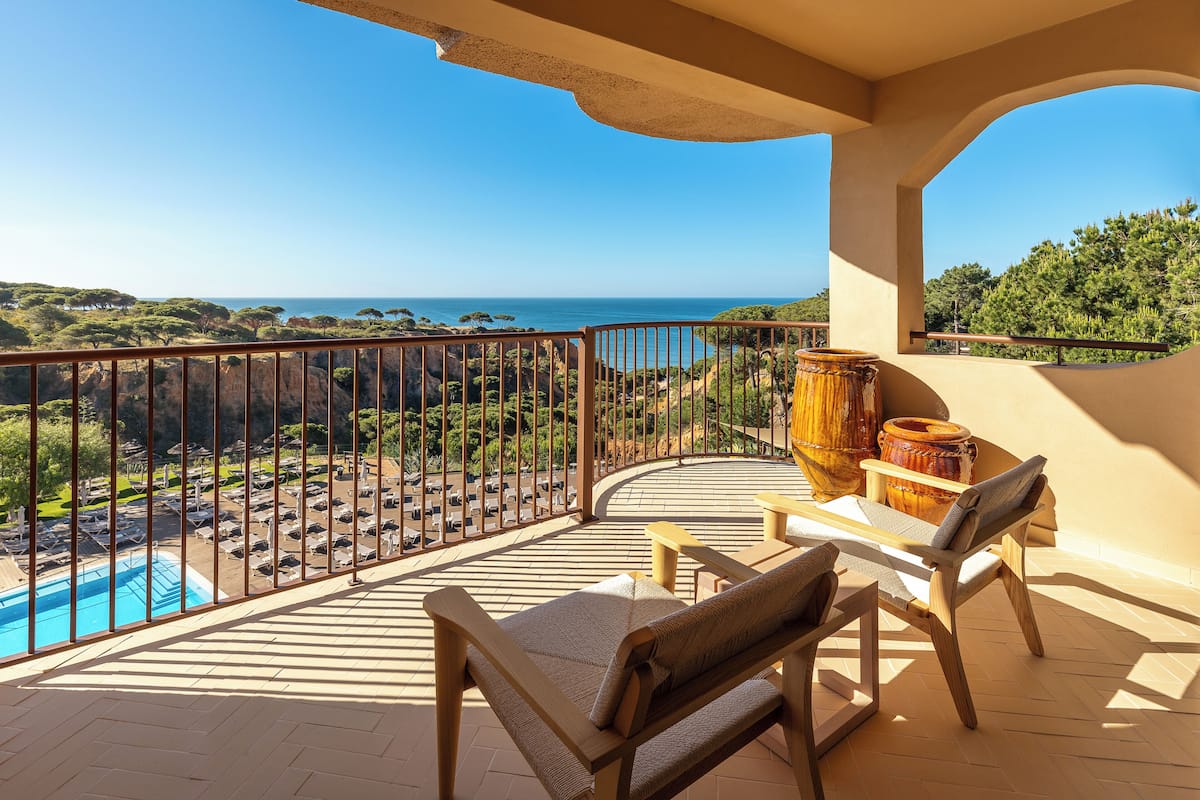 Un balcón con vista a la piscina, muebles de madera y vistas al océano.