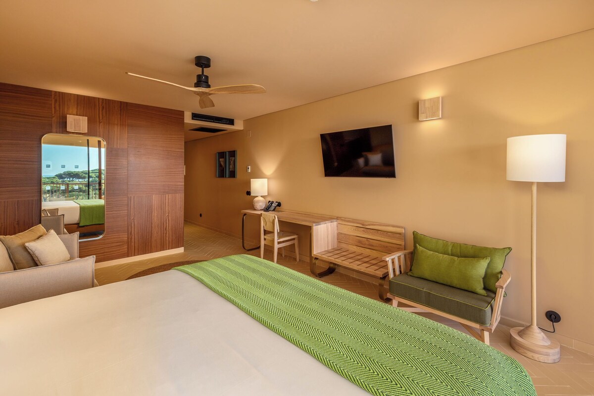 A hotel room with a large bed, a desk, a chair, a sofa, and a floor lamp.