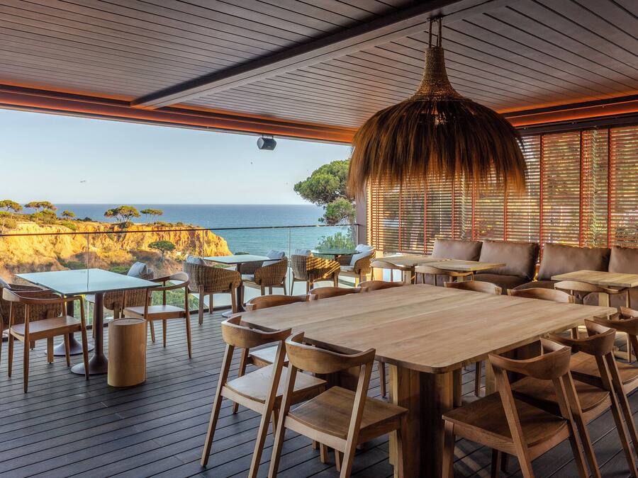 Une terrasse en bois, agrémentée de tables et de chaises, qui offre une vue sur un paysage côtier avec des falaises et la mer.