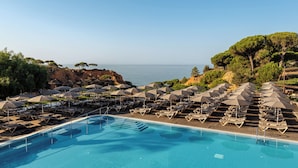 A poolside area with lounge chairs and umbrellas, overlooking a body of water and rocky terrain.