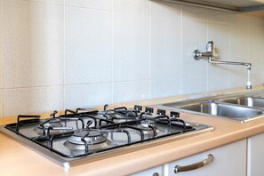 Een keuken met een gasfornuis, een spoelbak en een betegelde achterwand.