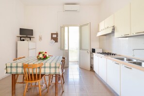 Une cuisine de taille réduite comprenant une table à manger, des chaises, un réfrigérateur, une cuisinière et des placards.