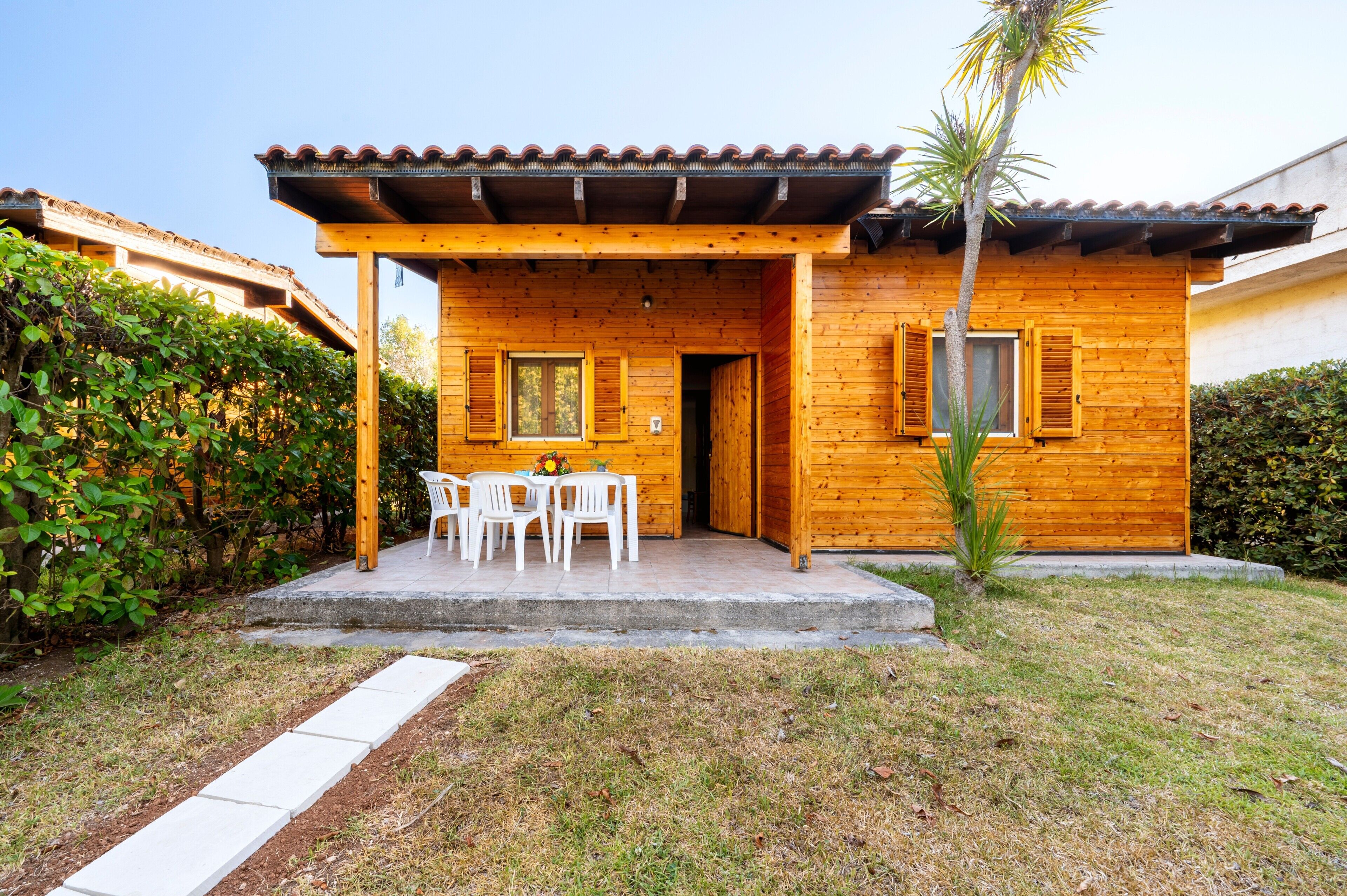 A wooden house with a covered patio, white chairs, and a small table.