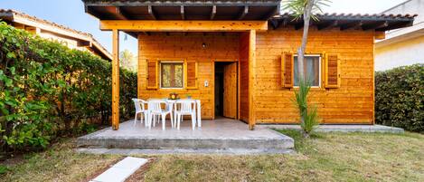 A wooden house with a covered patio, white chairs, and a small table.