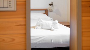 A neatly made bed with a white pillow and a folded towel, a bedside lamp, and a wooden wall panel.