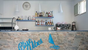 A bar area with a stone wall, shelves with bottles, a coffee machine, and a clock on the wall.