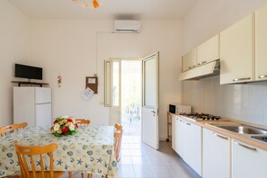 Una cocina compacta con zona de comedor, armarios blancos, una estufa y un televisor sobre un mueble.